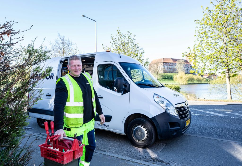 Laddbox Smiling worker in reflective vest stands by a van holding tools.